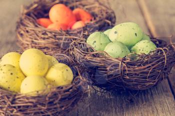 Three nests with painted eggs on wooden background. Close-up view with selective focus.
