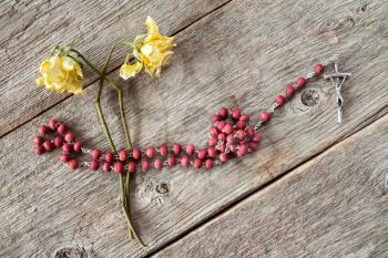 Catholic rosary and dry yellow roses on wooden background