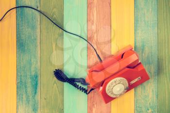 Orange rotary phone  on colorful wooden background. Top view.
