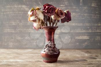 Bouquet of dry roses in a vase on wooden background