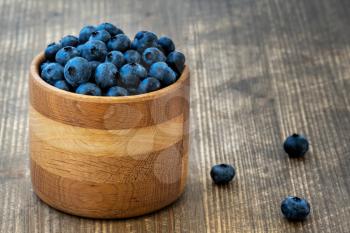 Freshly picked organic blueberries in wooden bowl on wooden background. Healthy eating and nutrition.