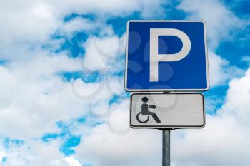 Standard disabled parking sign with clouds in the background