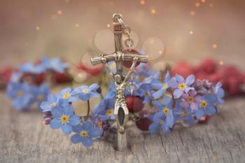 Christian cross on rosary and a blue flowers lie on a wooden table