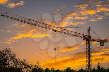 Silhouette of industrial construction tower crane against sunset sky on the background, real estate building development, architecture business concept work