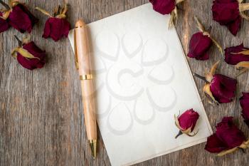 Blank paper with dry roses on wooden background. Love letter. Copy space.