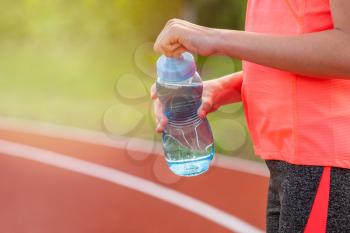 Thirst and water balance concept. Girl holding bottle of water on running track on the stadium.