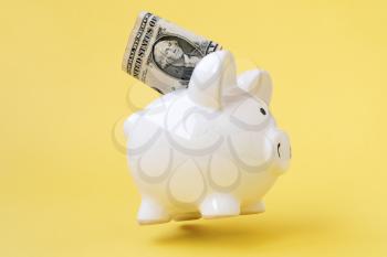 American currency in a piggy bank levitating over yellow background