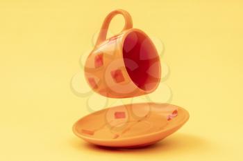 Empty orange color cup with plate falling on the yellow background
