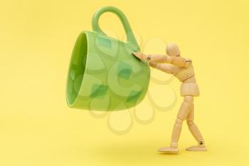 Wooden man holding green cup floating on yellow background
