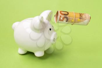 Piggy bank and roll of money floting over green background