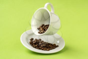 White cup filled with roasted coffee beans floating over a green background