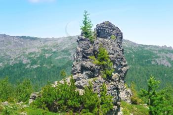 Royalty Free Clipart Image of a Single Rock With Trees Against Mountains