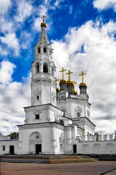 White Stone Holy Trinity church tower with gold baths and crosses against the blue sky, white clouds (Verhoturie city of Sverdlovsk Region)