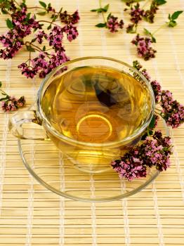 Herbal tea in a glass cup and saucer, oregano sprigs of flowers on a background of bamboo napkins