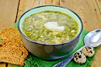Green soup of sorrel, nettle and spinach in a bowl, quail eggs, bread, pepper, spoon on a background of wooden boards