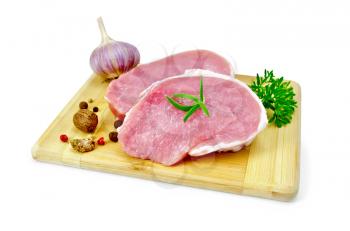 Two slices of pork, garlic, nutmeg, parsley, rosemary and pepper on a wooden board isolated on white background