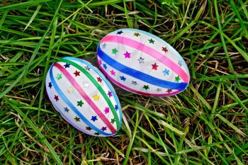 Two easter eggs, decorated with multicolored braid and sparkles as asterisks on green grass top