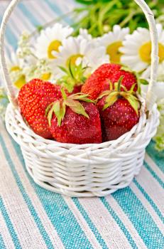 Ripe red strawberries in a white wicker basket, a bouquet of chamomile on a background of green striped napkin