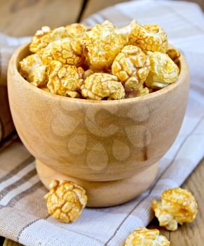 Caramel popcorn in a wooden bowl on a napkin on the background of wooden boards