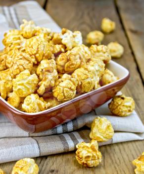 Caramel popcorn in a clay bowl with a napkin on a wooden boards background