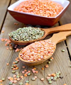 Red and green lentils in a wooden spoon and a clay bowl on a wooden boards background