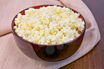 Cottage cheese in a wooden bowl on a napkin on the background of wooden boards