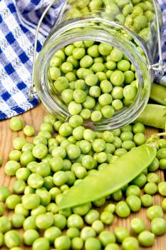 Green peas in glass jar, blue checkered napkin on the background of wooden boards