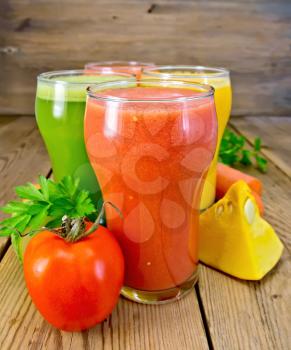 Four tall glasses with juice tomato, carrot, cucumber and pumpkin, vegetables on the background of wooden boards