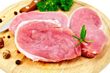 Three chunk of pork, nutmeg, parsley, rosemary and pepper on a round wooden board isolated on white background