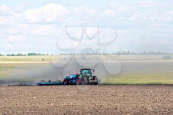Blue wheeled tractor working on the background of plowed land, cereals and sky
