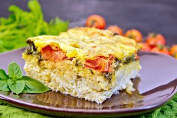 The pie of potatoes, cheese, tomato and spinach, filled egg with milk in a plate, a napkin against a wooden board