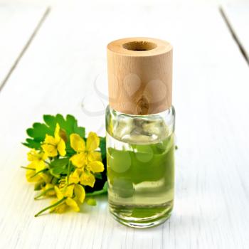 Oil in a bottle, flowers and leaves of celandine in the background light wooden boards
