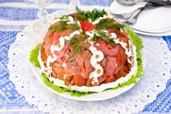 Salad layered with salmon, egg, crab meat and rice, mayonnaise in a plate on a green lettuce on the background of a blue tablecloth