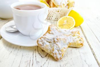 Cookies lemon, tea in a white cup on saucer, lemons on a background of wooden boards