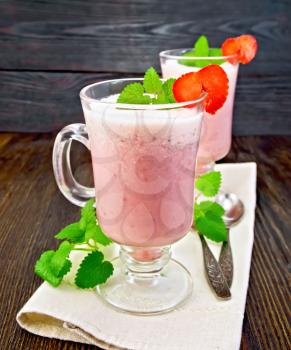 Strawberry soup in two glass goblets with berries and mint and spoon on a napkin on a dark wooden board