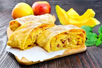 Strudel pumpkin and apple with raisins on parchment, mint, fruit and vegetables on a dark wooden board