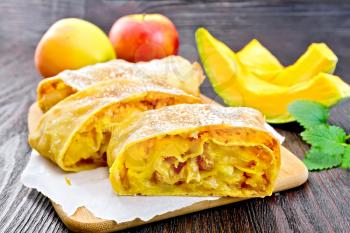 Strudel pumpkin and apple with raisins on parchment, mint, fruit and vegetables on the background of wooden boards