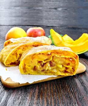 Strudel pumpkin and apple with raisins on paper, pine branches with Christmas toys in the background of a wooden board