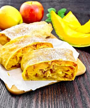 Strudel pumpkin and apple with raisins on parchment, fruits and vegetables on a wooden boards background