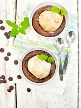 Two white bowl dessert with chocolate and pear, spoon, mint on a towel on the background of the wooden planks on top