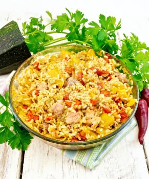 Rice with chicken, tomatoes, carrots, zucchini and garlic in a glass pan on a napkin, parsley and chili peppers on a wooden boards background