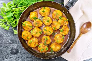 Meatballs with tomato sauce in a frying pan with parsley, dill, napkin and spoon on a wooden board background