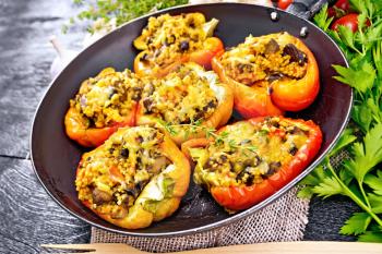 Pepper sweet, stuffed with mushrooms, tomatoes, couscous and cheese in an old frying pan on burlap, a fork, garlic, parsley and thyme against the background of dark wooden board