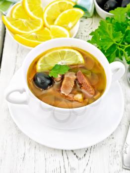 Soup saltwort with lemon, meat, pickles, tomato sauce and olives in a white bowl on a light wooden board background