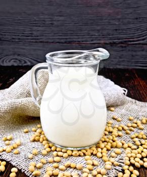 Soy milk in a jug, soybeans on a napkin of burlap on the background of a dark wooden board