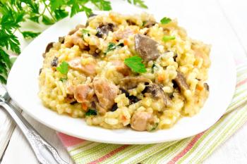 Rice risotto with mushrooms, chicken meat, cheese and garlic in a plate on a towel, fork and parsley on a wooden board background