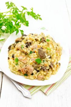 Rice risotto with mushrooms, chicken meat, cheese and garlic in a plate on a kitchen towel, fork and parsley on a wooden board background