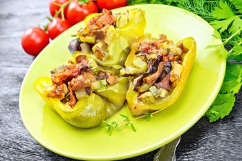 Sweet pepper stuffed with mushrooms, tomatoes, zucchini, eggplant and onions, seasoned with wine, garlic, thyme and spices in a green plate against dark wooden board