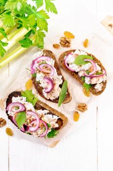Salmon, petiole celery, raisins, walnuts, red onions and curd cheese salad on toasted bread with green lettuce on paper on a light wooden board background from above