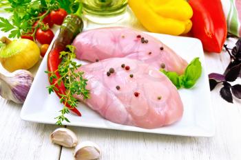 Chicken breast with hot pepper and thyme in a plate, towel, parsley and basil, onion, garlic and vegetables on a wooden board background
